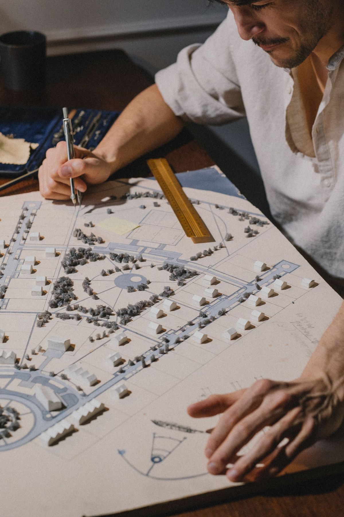 A designer working over a scaled site plan with a compass and scale rule