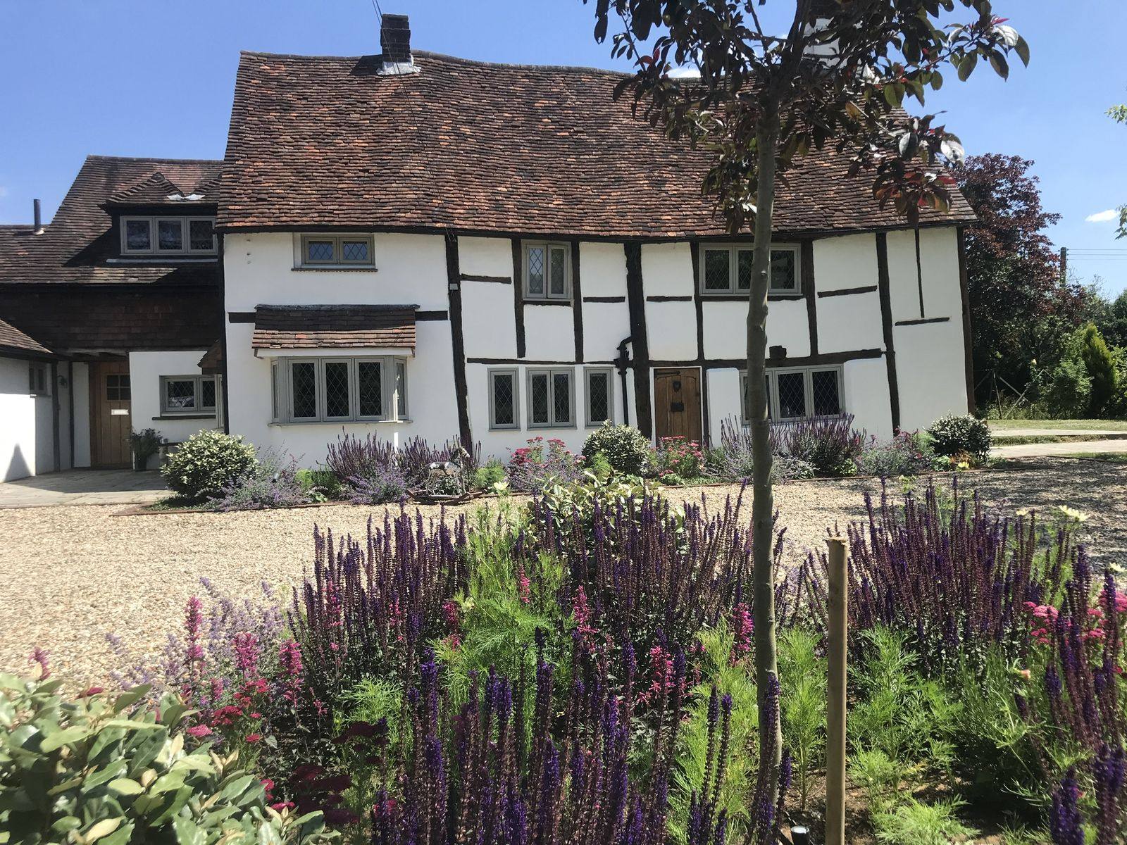 New frontage planting to a timber-framed house: salvia, achillea and lavender in a gravel island, keeping the drive usable and the elevation visible.